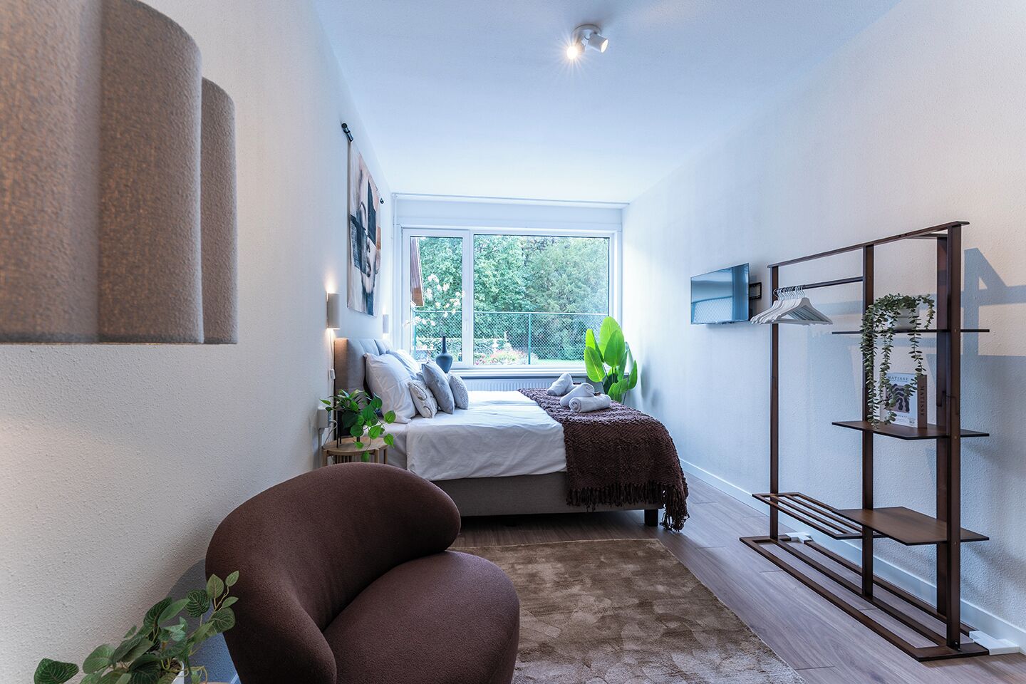 A modern bedroom with a bed, a large window, a plant, and a wooden bench.