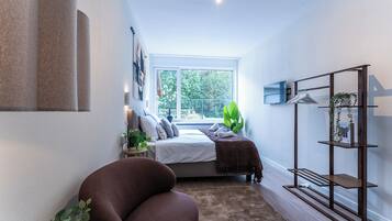 A modern bedroom with a bed, a large window, a plant, and a wooden bench.