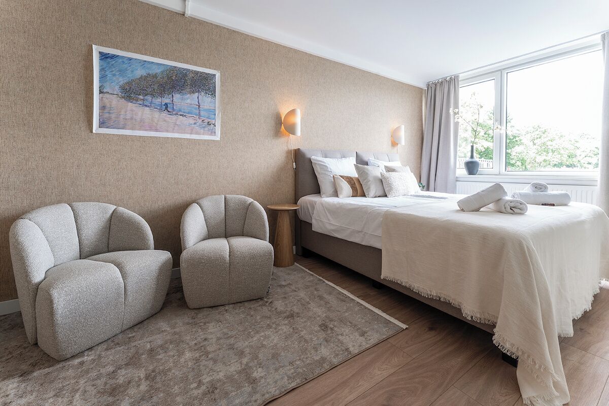 Una habitación de hotel con cama, dos sillones, una mesita y un cuadro en la pared.