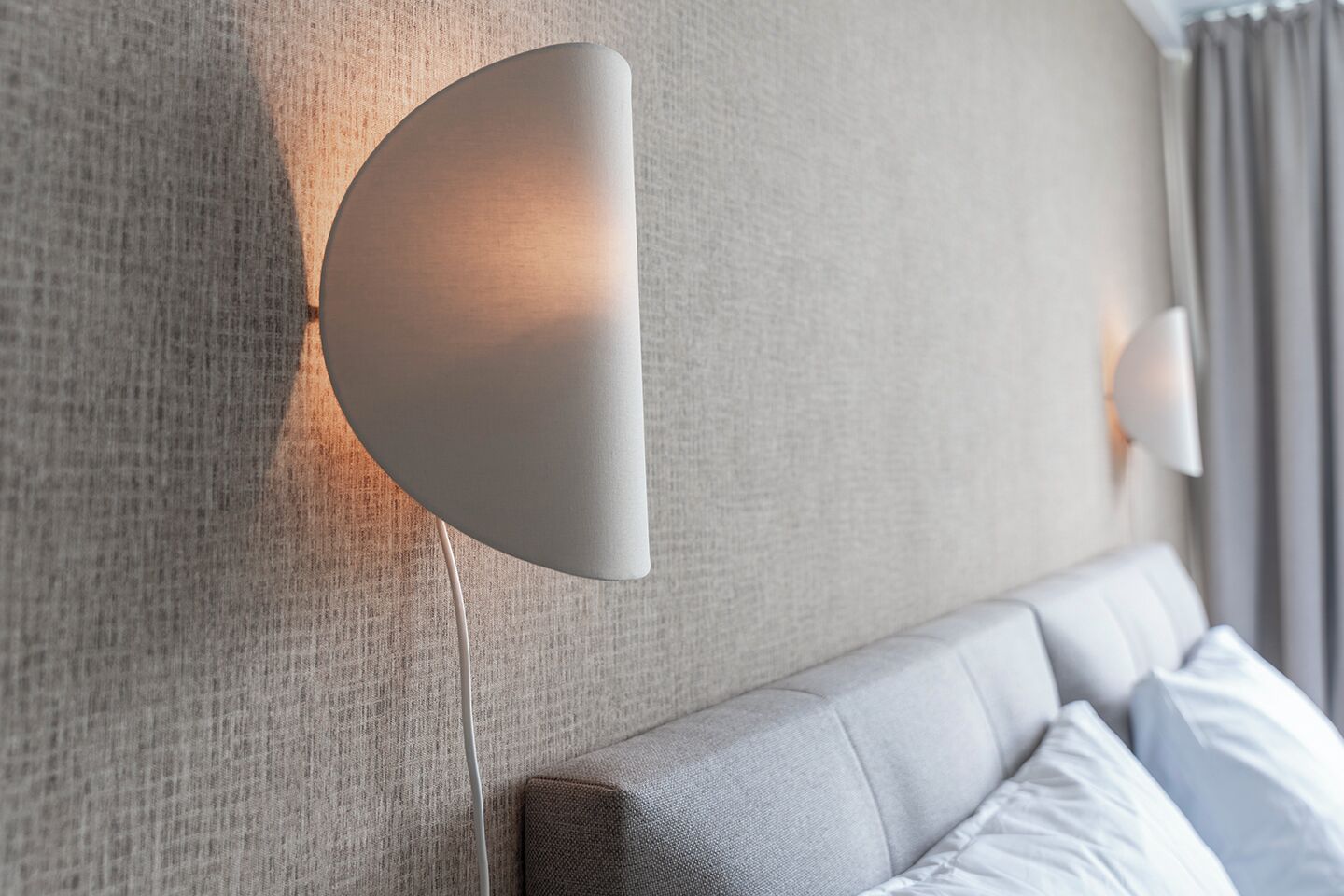 Una habitación de hotel moderna con una pared texturizada, una lámpara de pared curva y una cama ordenada con almohadas.