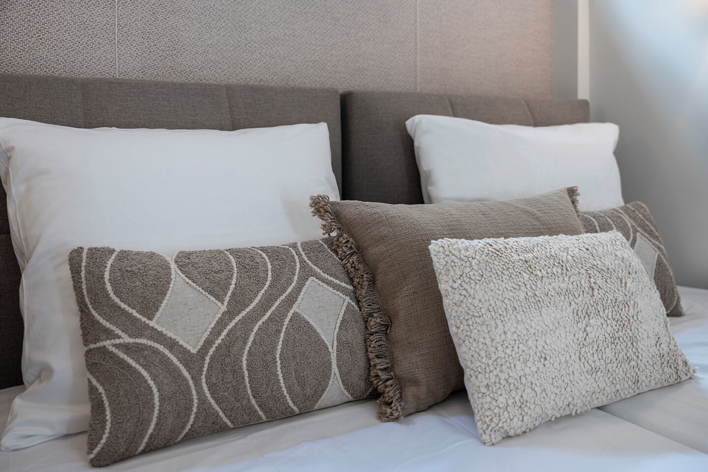 Una cama con cuatro almohadas de distintos diseños y texturas.