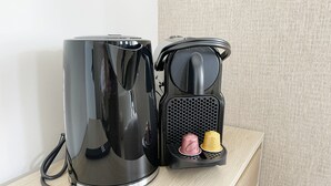 Une machine à café noire, dotée d’un réservoir d’eau et de deux dosettes de café, est posée sur une étagère en bois.