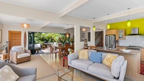 A spacious living area with a sofa, a glass coffee table, and a dining area with chairs and a table. - The Zen House - Our Island (Waiheke Island)