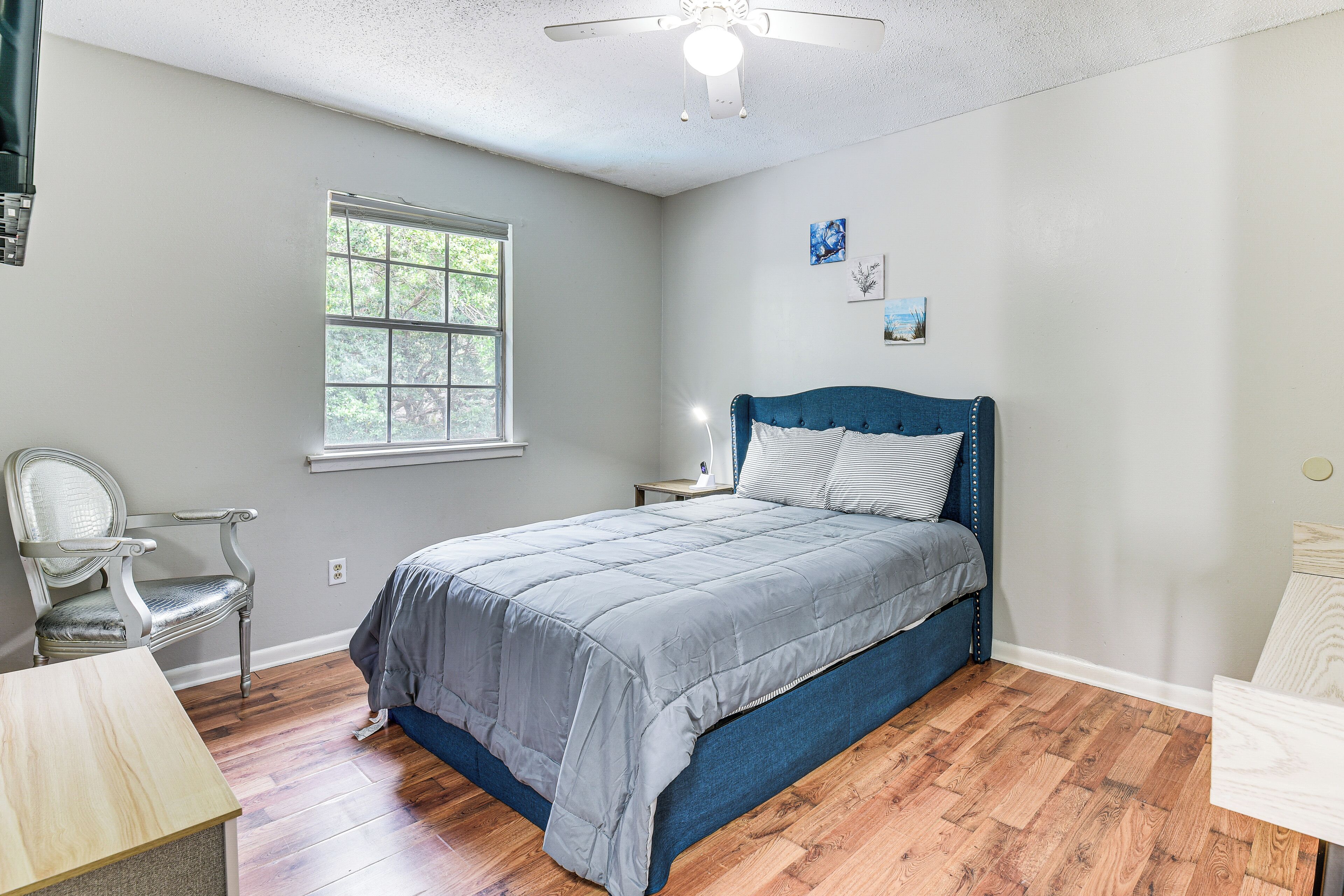 A bedroom with a bed, a chair, a nightstand, and a window.