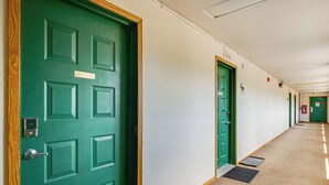 Un pasillo con puertas verdes, un felpudo y piso cubierto de alfombra.