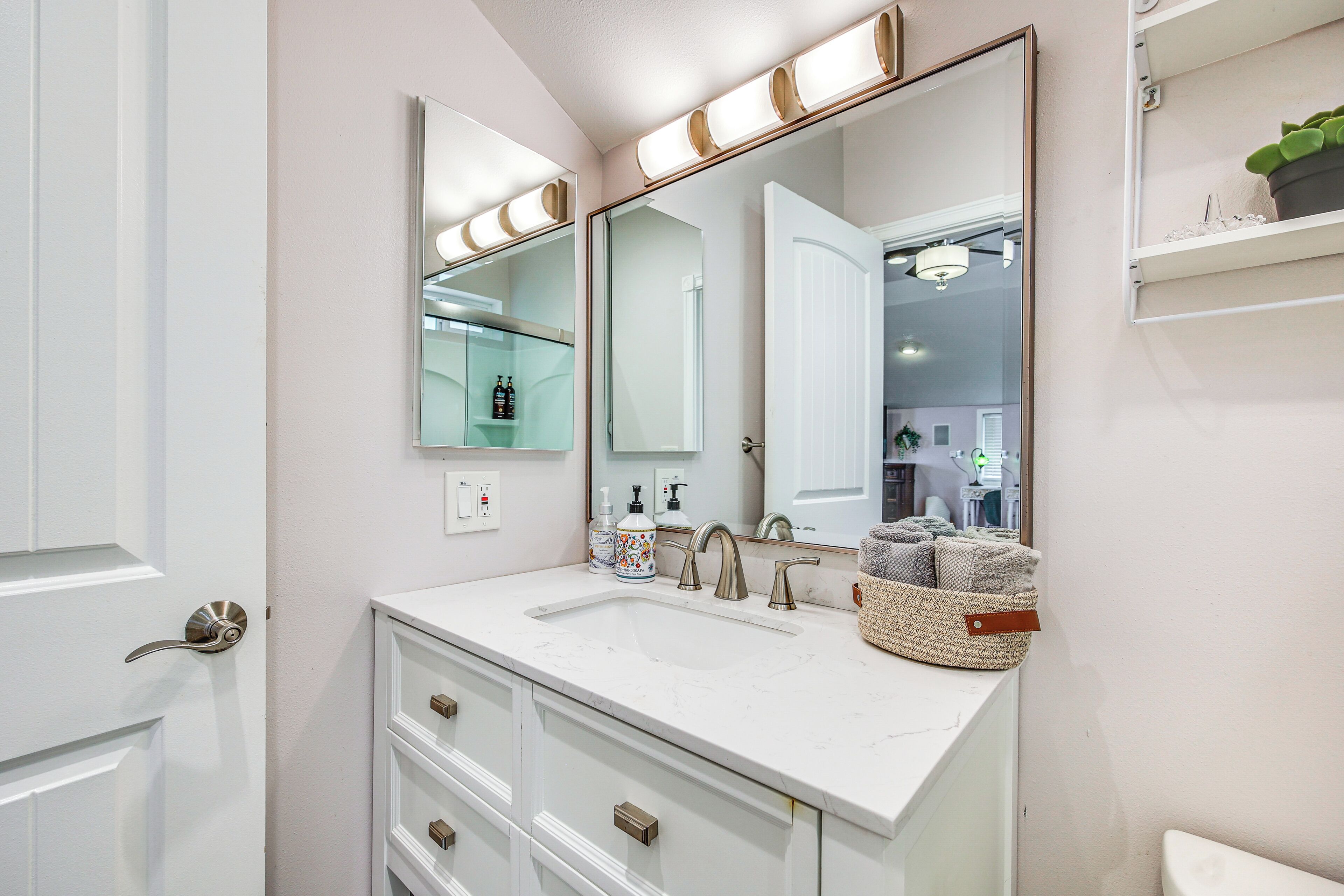A bathroom with a white vanity, a large mirror with lights, a sink, and a towel rack.