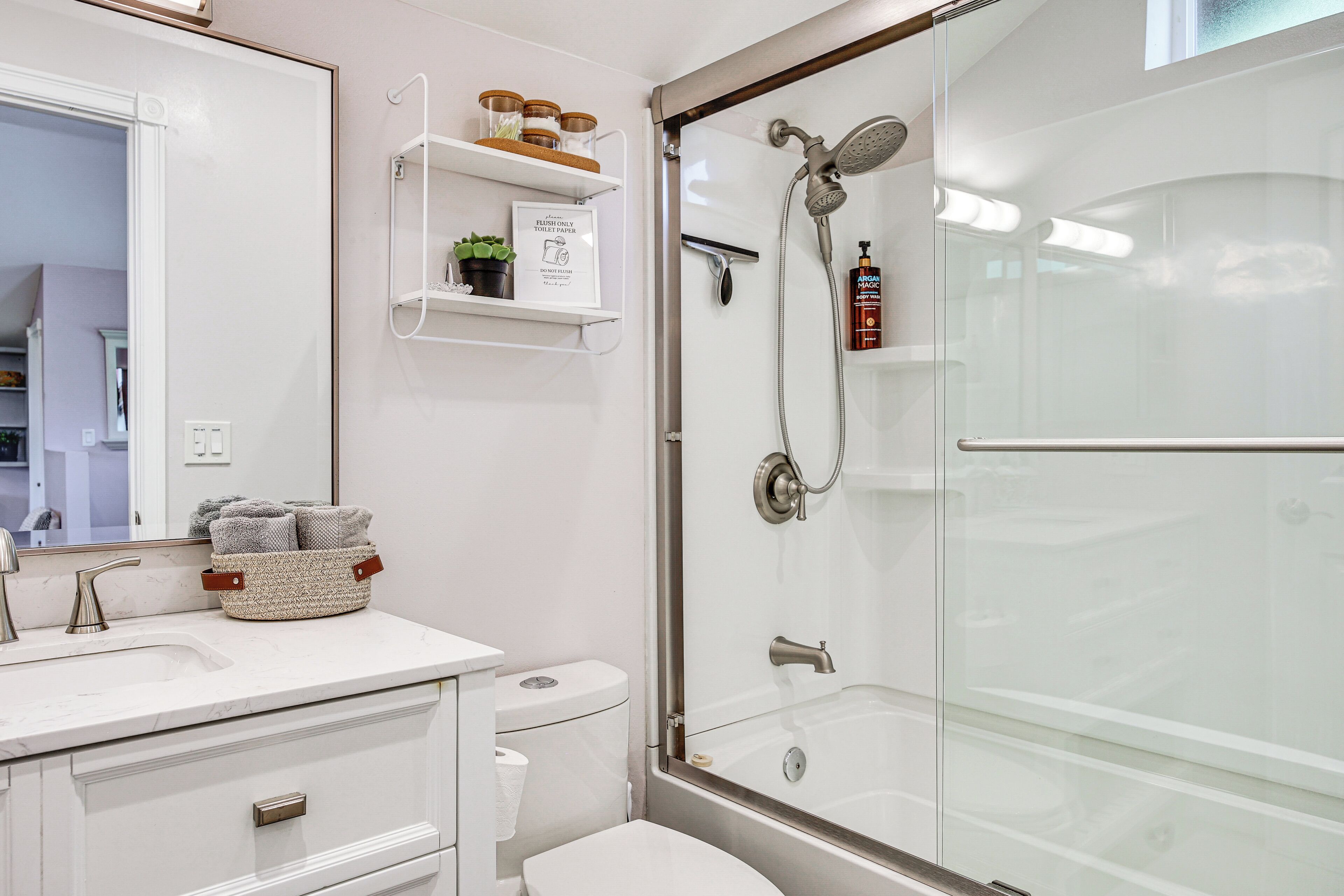 Un baño con cabina de ducha de vidrio, un lavamanos blanco con encimera de mármol, un inodoro y un espejo sobre el lavamanos.