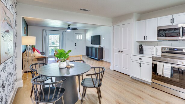 A modern kitchen with white cabinets, a stainless steel oven, and a dining area with a round table and chairs. - 1 Mi to Texas Tech: Home w/ Large Outdoor Space! (Lubbock)