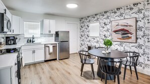 A modern kitchen with white cabinets, stainless steel appliances, and a dining area with a dark table and chairs. - 1 Mi to Texas Tech: Home w/ Large Outdoor Space! (Lubbock)