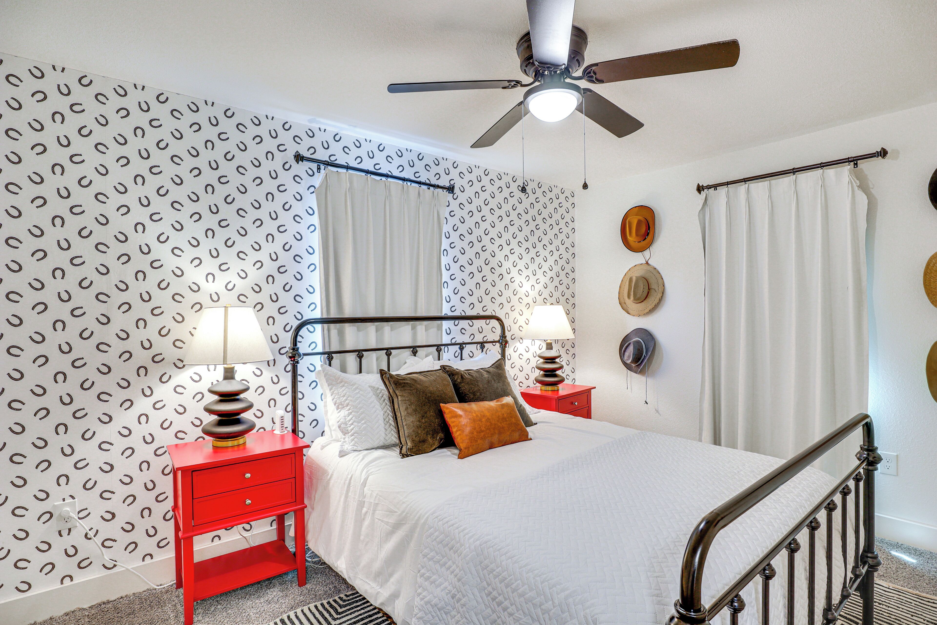 A neatly arranged bedroom with a bed, two bedside tables, a ceiling fan, and patterned wallpaper.