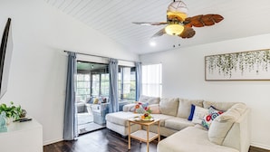 A modern living room with a sofa, a coffee table with fruit, and a ceiling fan. - 'wandering Waves!' w/ Private Beach & Pool Access (St. Augustine)