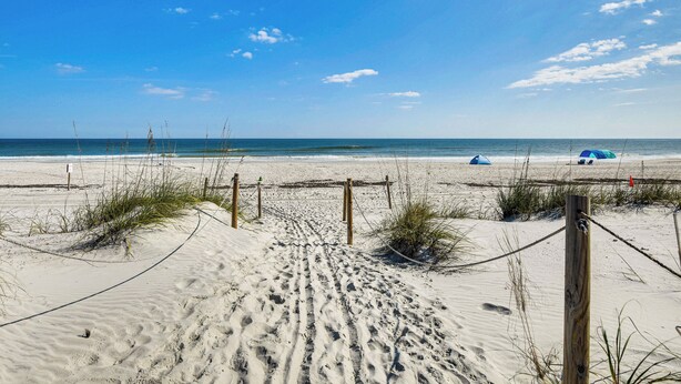 A sandy beach with footprints leading to the water, a wooden fence, and a tent in the distance. - 'wandering Waves!' w/ Private Beach & Pool Access (St. Augustine)