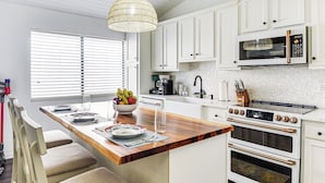 A modern kitchen with white cabinetry, a wooden island, a built-in oven, and a microwave. - 'wandering Waves!' w/ Private Beach & Pool Access (St. Augustine)