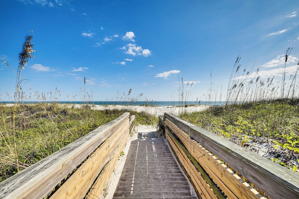 Une promenade en bois qui mène à une plage bordée de dunes de sable et dotée d’une végétation clairsemée.