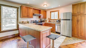 A spacious kitchen with wooden cabinets, a stainless steel refrigerator, and a large island with bar stools. - Walk to River: Couples Retreat in Kintnersville! (Kintnersville)