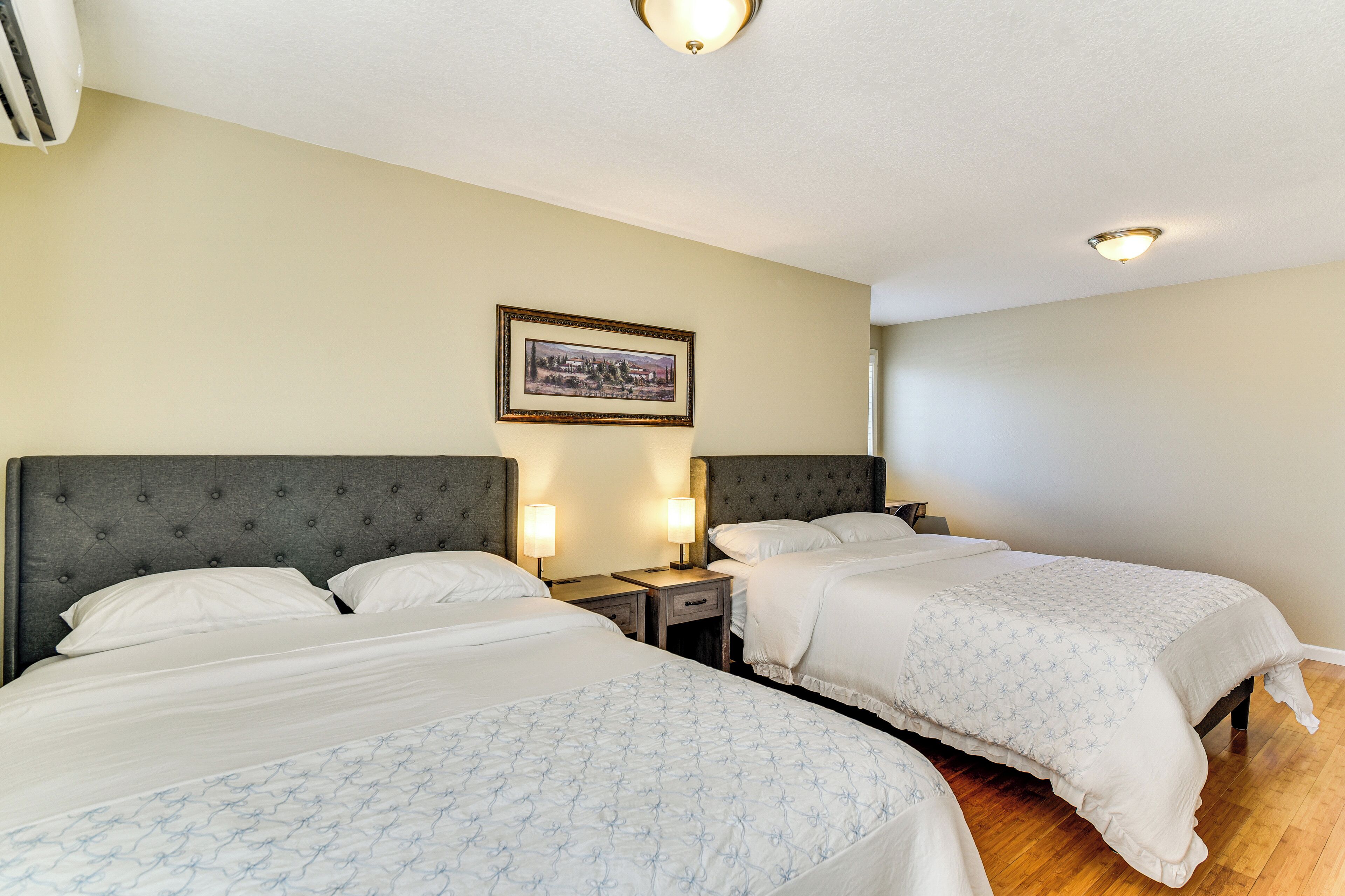 Quarto de hotel com duas camas, um quadro na parede e uma luminária no teto.