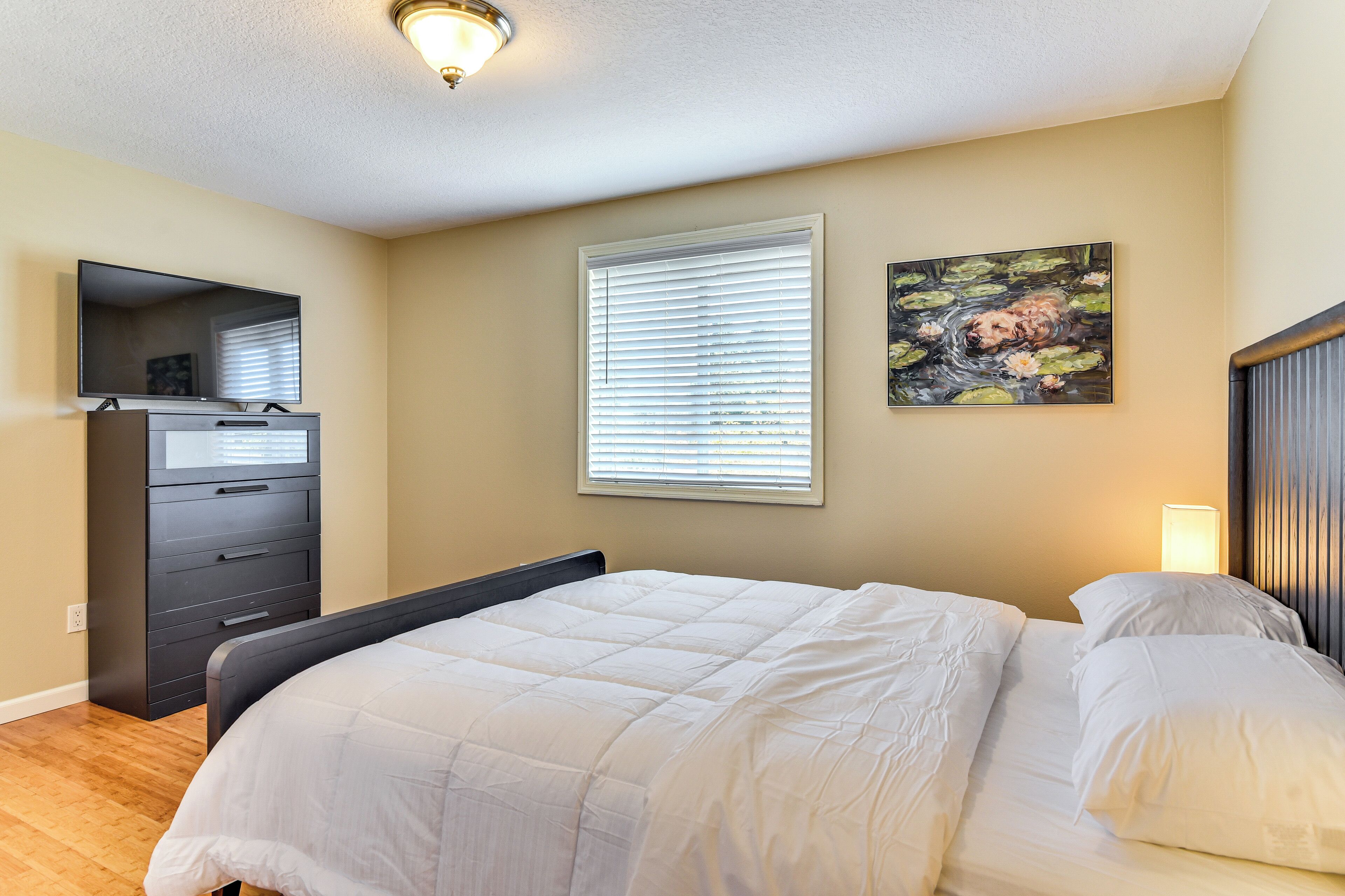 Une chambre à coucher avec un lit, une commode, un téléviseur et une fenêtre avec des stores.