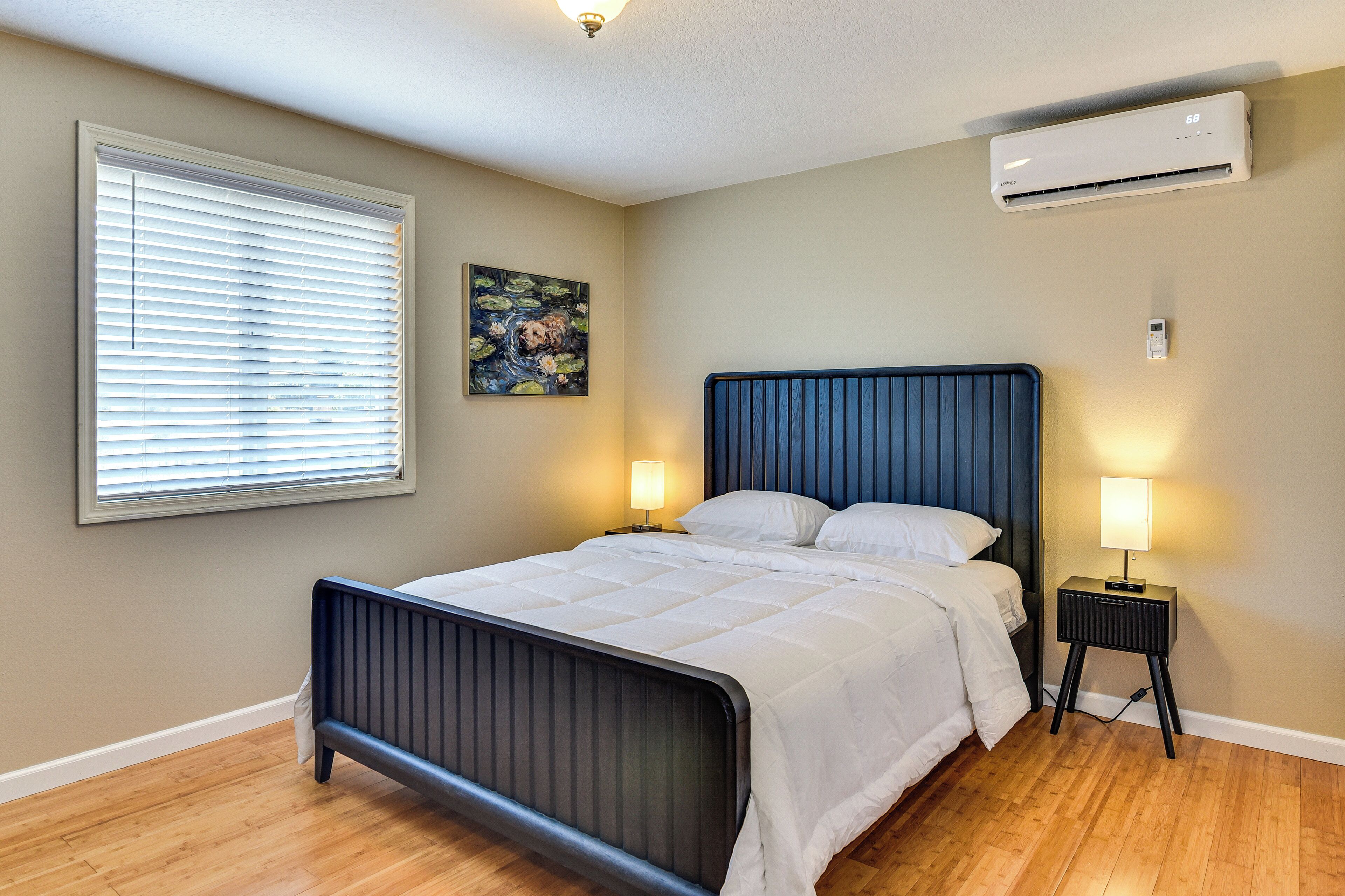 Un dormitorio con cama, lámparas de noche, aire acondicionado y una ventana con persianas.
