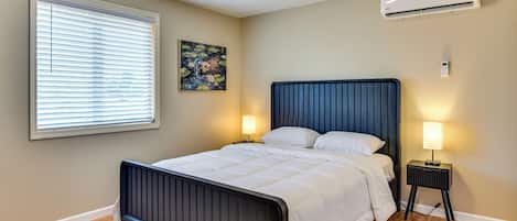 Un dormitorio con cama, lámparas de noche, aire acondicionado y una ventana con persianas.