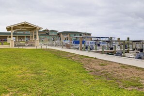 Un hotel frente al agua con una terraza cubierta, un muelle para embarcaciones y un césped.