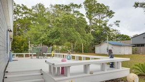 A wooden deck with steps leading to a white picnic table surrounded by potted plants and a small garden area with rocks and a large decorative ball.