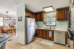 Una cocina con armarios de madera, un refrigerador de acero inoxidable, un lavavajillas y un comedor con mesa y sillas.