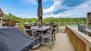 Une terrasse en bois avec des meubles d’extérieur, une table couverte et une vue sur un lac et une forêt.
