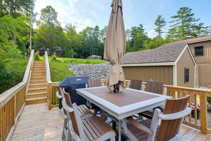 A wooden deck with a table and chairs, a barbecue grill, and a covered umbrella. - Waterfront Haven Bi-level Lakefront Deck/game Cntr (Fort Ann)