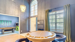 A room with a round table, four chairs, a bench, a wall-mounted TV, a door, and a window with curtains. - Group-friendly Grand Prairie Home w/ Perks! (Grand Prairie)
