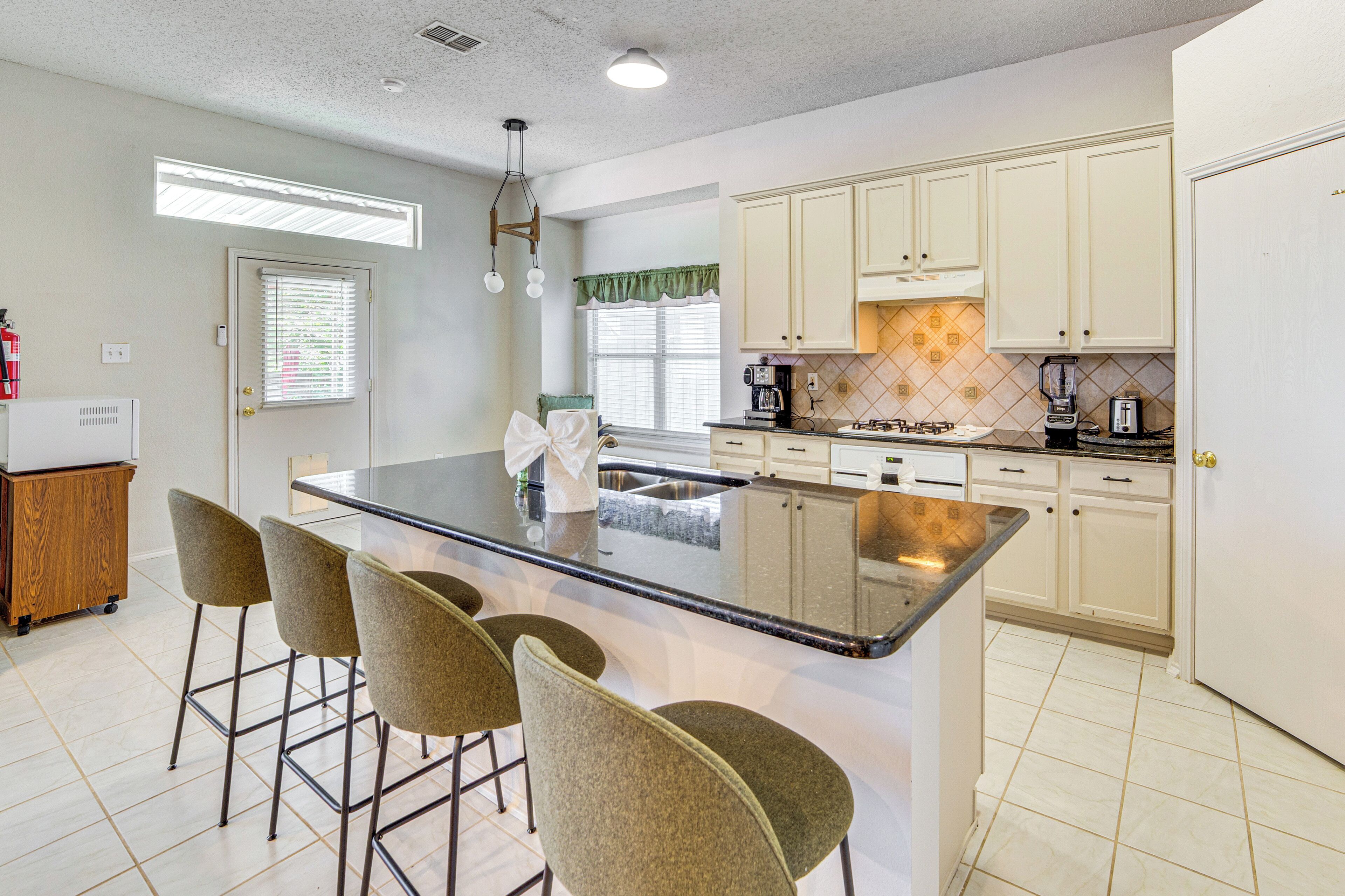 A kitchen with a central island, bar stools, and white cabinets.