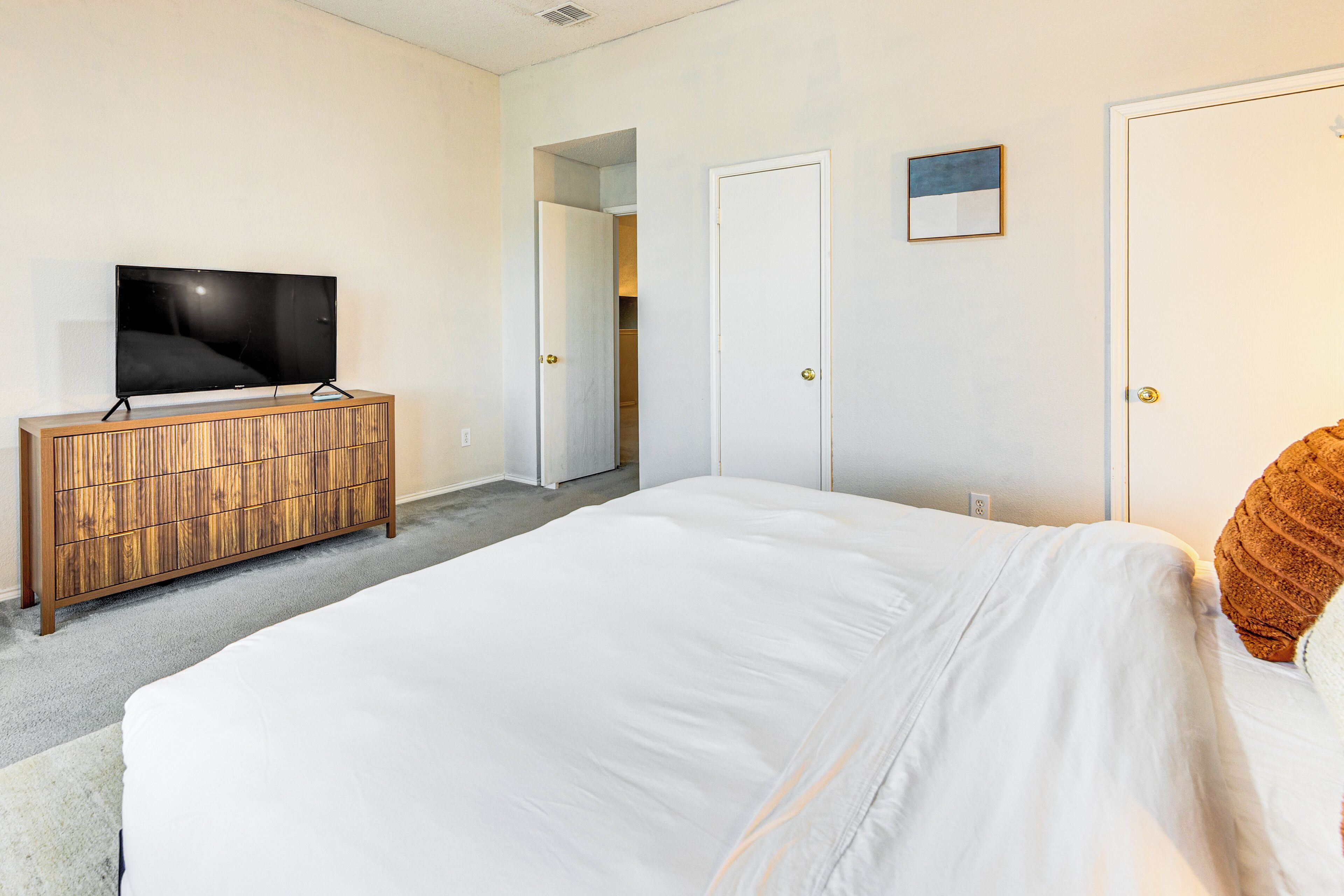 A bedroom with a bed, a TV on a wooden dresser, and two doors.
