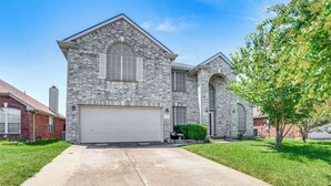A two-story house with a garage, a brick exterior, and a well-maintained lawn. - Group-friendly Grand Prairie Home w/ Perks! (Grand Prairie)