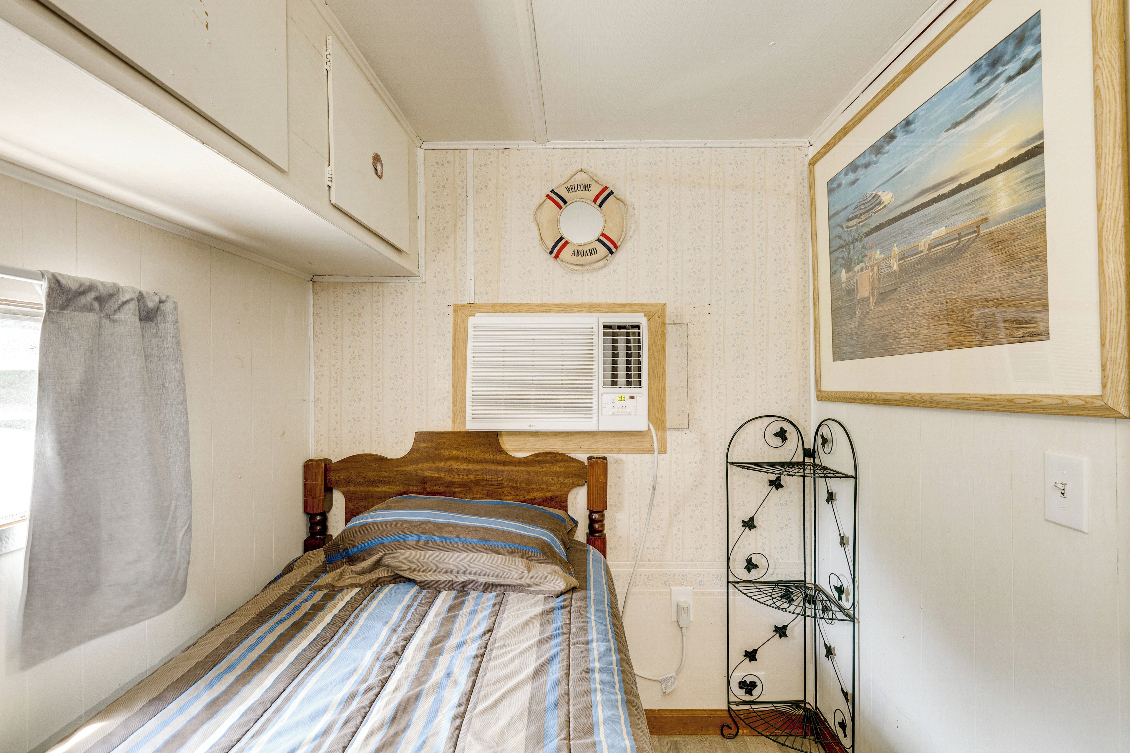 Une chambre avec un lit, un climatiseur fixé au mur, une pancarte de bienvenue et un tableau représentant une scène de plage.
