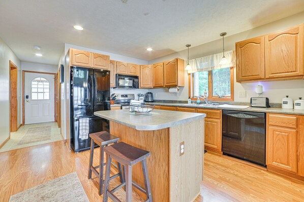 A modern kitchen with wooden cabinets, stainless steel appliances, and a central island with stools.