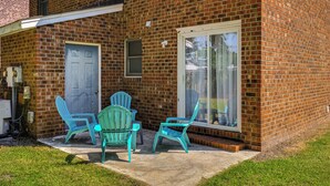 A brick house with a patio area featuring two green Adirondack chairs and a small table.