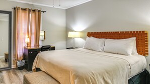 A hotel room with a large bed, a desk with a chair, a lamp, and a mirror.