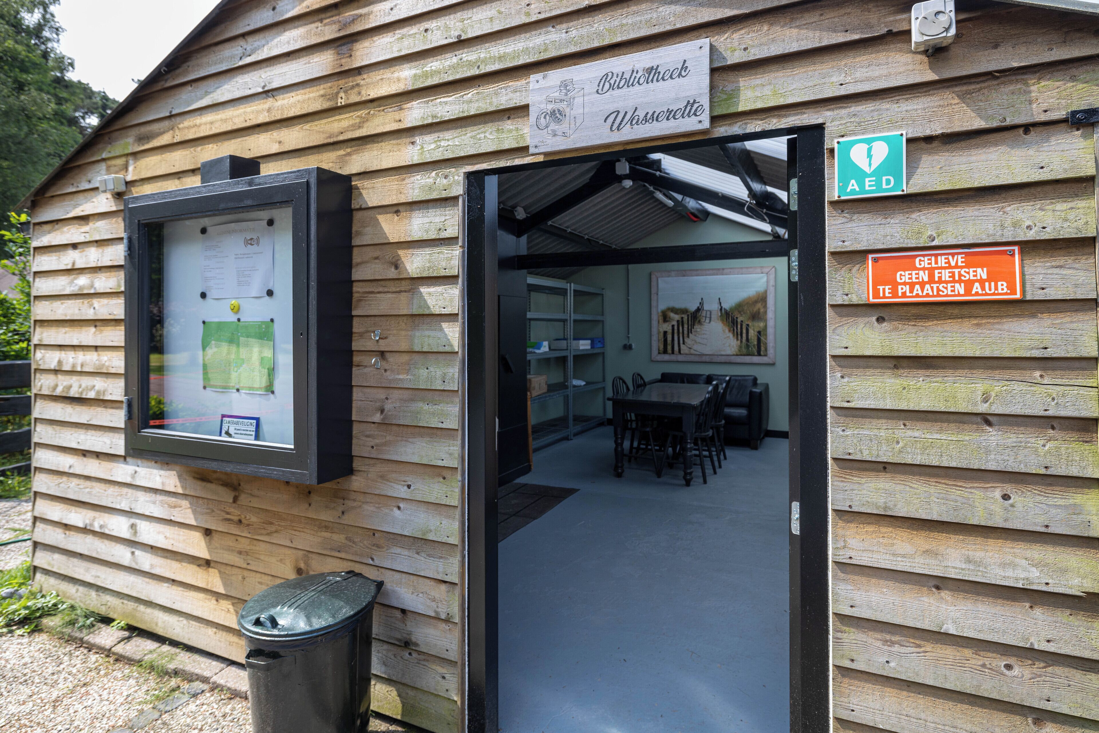 A wooden building with a sign reading "Bibliotheek Wasserette" and an AED sign.