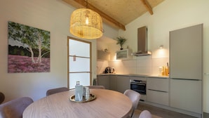 A modern kitchen with a round dining table, pendant light, and a painting of trees. - Geniet samen van de rust en natuur (Giethmen)