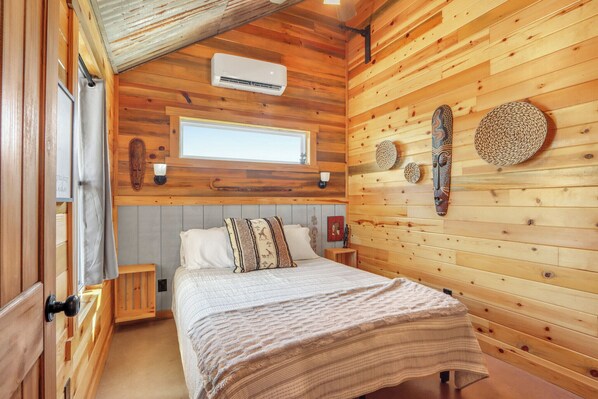 A wooden cabin bedroom with a bed, a window, and a wall-mounted air conditioner.