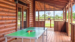 Un terrazzo in legno con tavolo da ping pong, un mulino a vento sullo sfondo e una zona coperta con una ventola a soffitto.