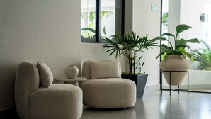 A modern lobby with two round beige sofas, a small table, and potted plants. - Modern Apt | 4BR | Marina & Beach Access (Cancún)