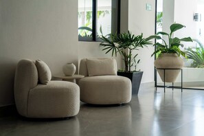 Un hall moderno con dos sillones beiges redondeados, una mesita y plantas en macetas.
