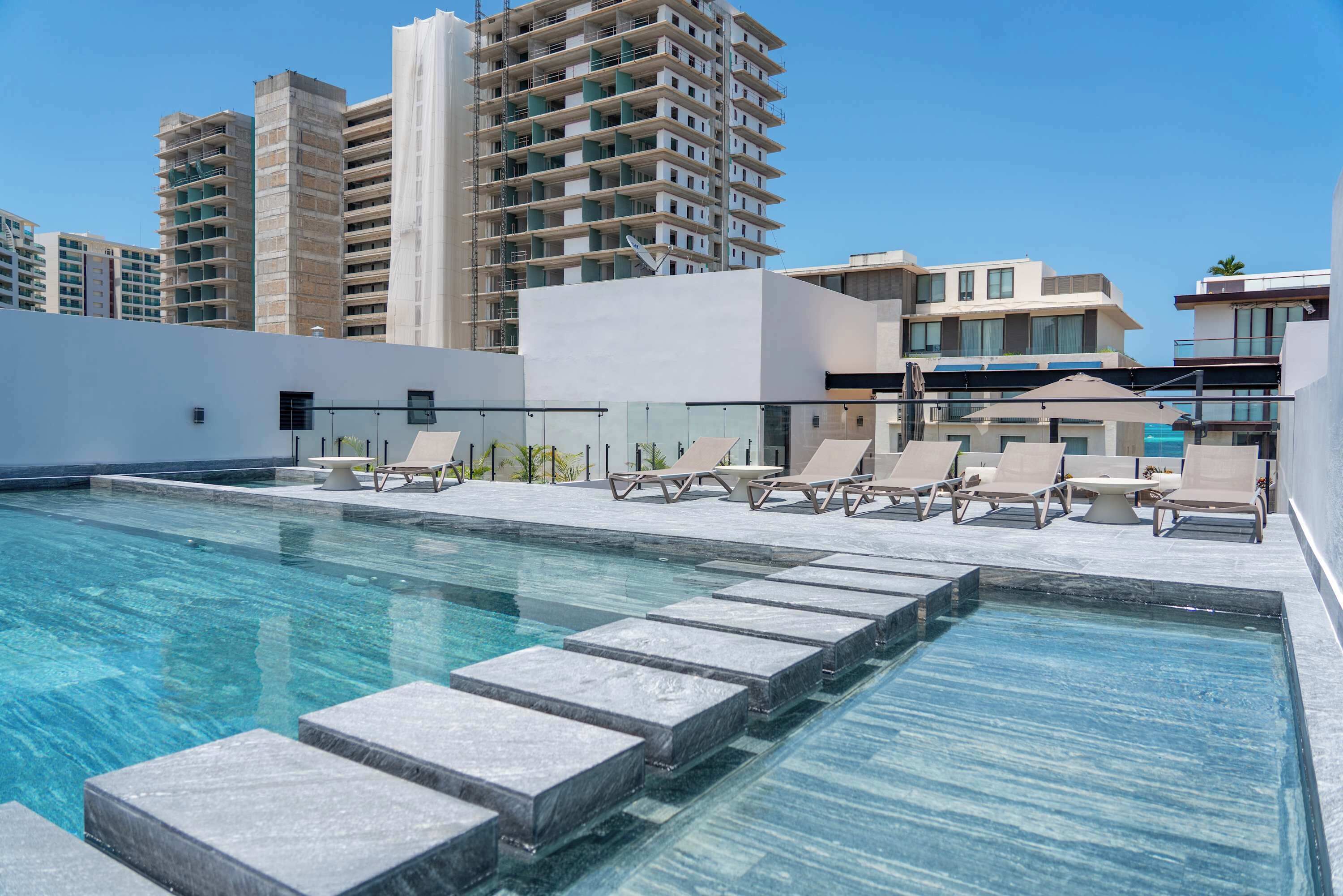 A rooftop pool with lounge chairs and a clear view of surrounding high-rise buildings.