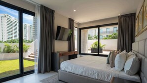 A modern bedroom with a large bed, a flat-screen TV, and a view of a cityscape through large windows. - Modern Apt | 4BR | Marina & Beach Access (Cancún)