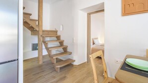 En modern inredning med en trätrappa, en säng med ett grönt sänggavel och en matplats med ett bord och stolar.