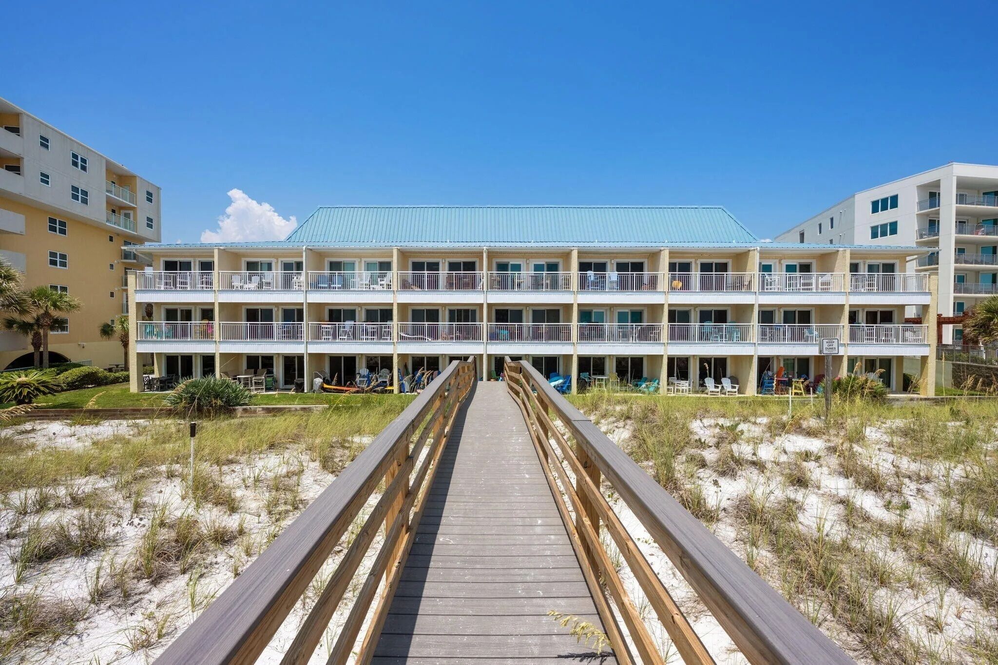 Ein Strandhotel mit einer Holzpromenade, die zu einem Gebäude mit mehreren Balkonen und Außenbereichen zum Sitzen führt.