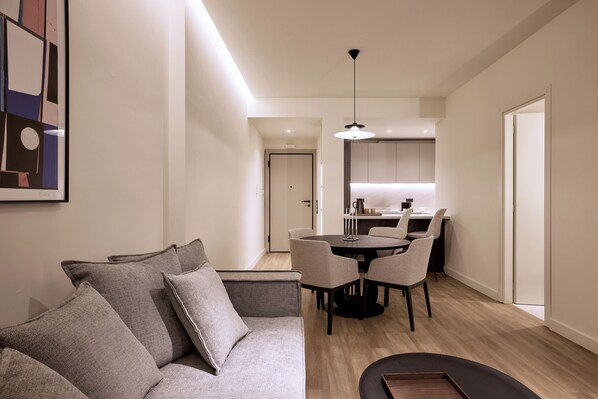 Una sala de estar moderna con un sofá gris, una mesa de comedor con sillas y una cocina al fondo.