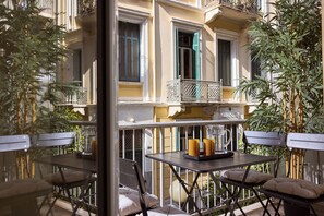 Ein Außenbereich mit Tischen und Stühlen, ein Balkon mit Geländer sowie ein Gebäude mit Fenstern und Fensterläden.