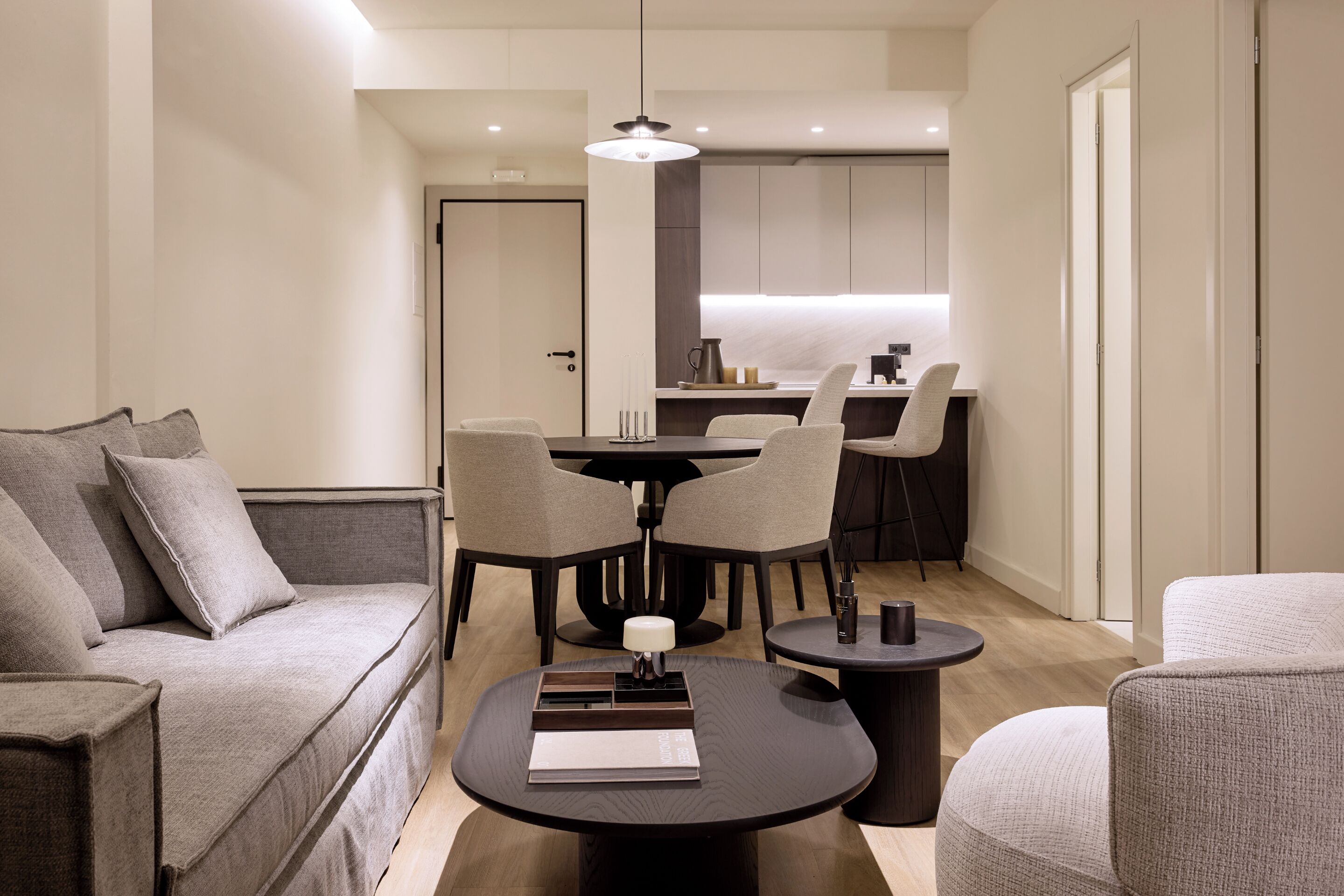 Una sala moderna con un sofá, dos sillones, una mesa de centro y un comedor con una mesa y sillas.