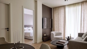 Een moderne hotelkamer met een bed, een zithoek met een ronde tafel, en een aan de muur bevestigde televisie.
